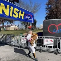 A volunteer carrying a child near the finish line banner