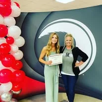 Two women posing with a race award and balloon arch
