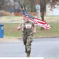 A soldier running the course with a large American flag